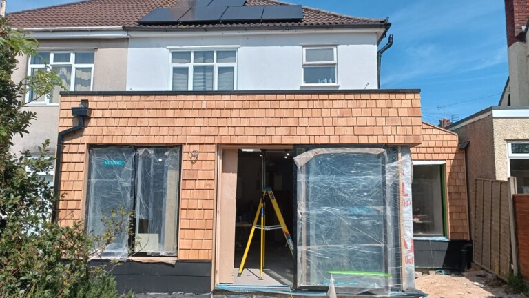 A newly clad rear extension with cedar shingles around a window and sliding door