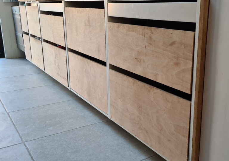 Ten Ikea Kitchen drawers customised with plywood inners wait for the final drawer fronts to be fitted. With Large format porcelain floor tiles.